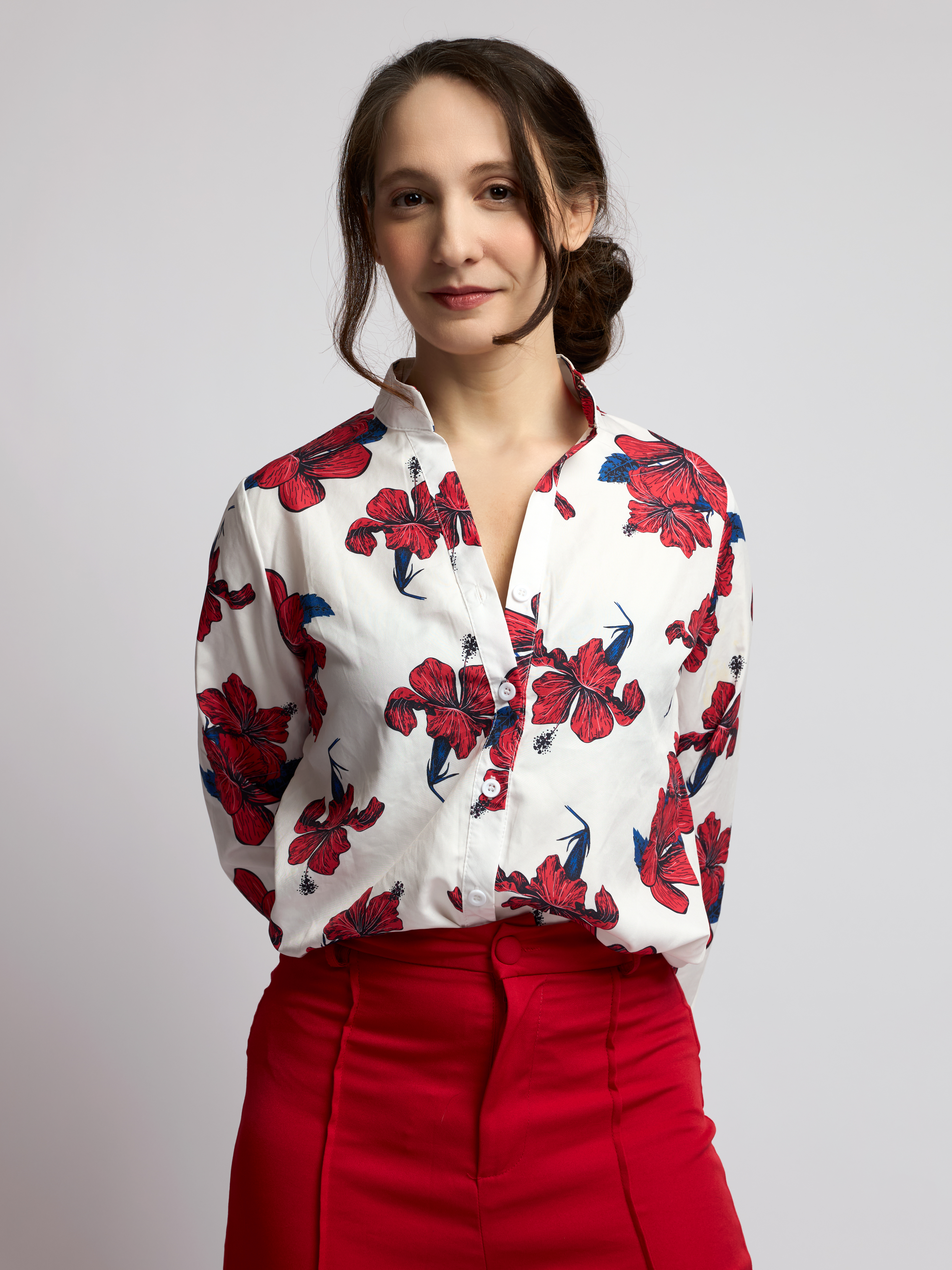 Female model in a white floral-print blouse and red skirt posing against a soft grey studio background